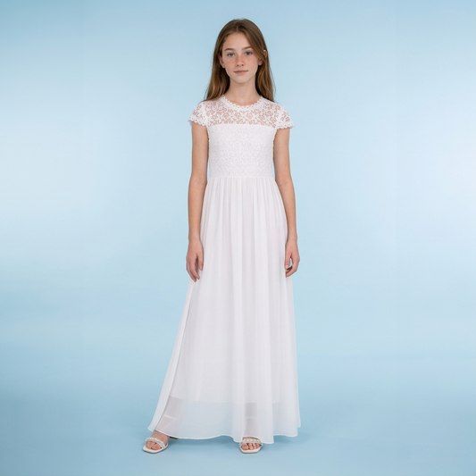 A young girl modeling a long white maxi dress with a lace bodice and cap sleeves, standing against a light blue studio background.
