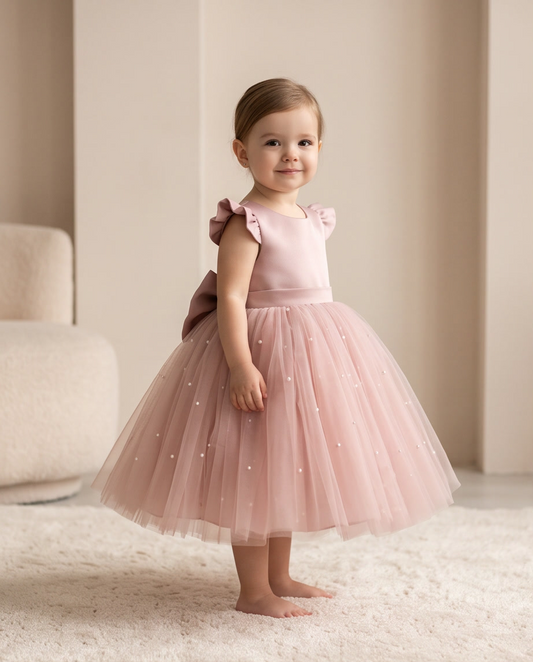Toddler girl wearing blush pink pearl tulle dress full length front view on white rug