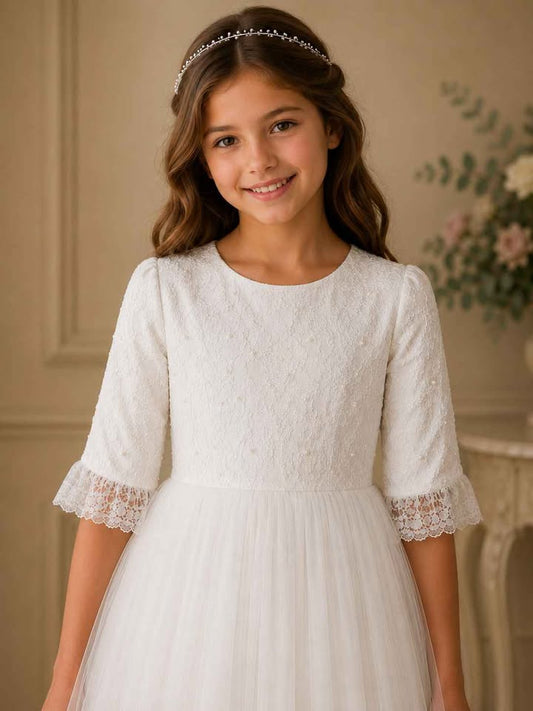 Young girl wearing a white lace dress with a tiara indoors.