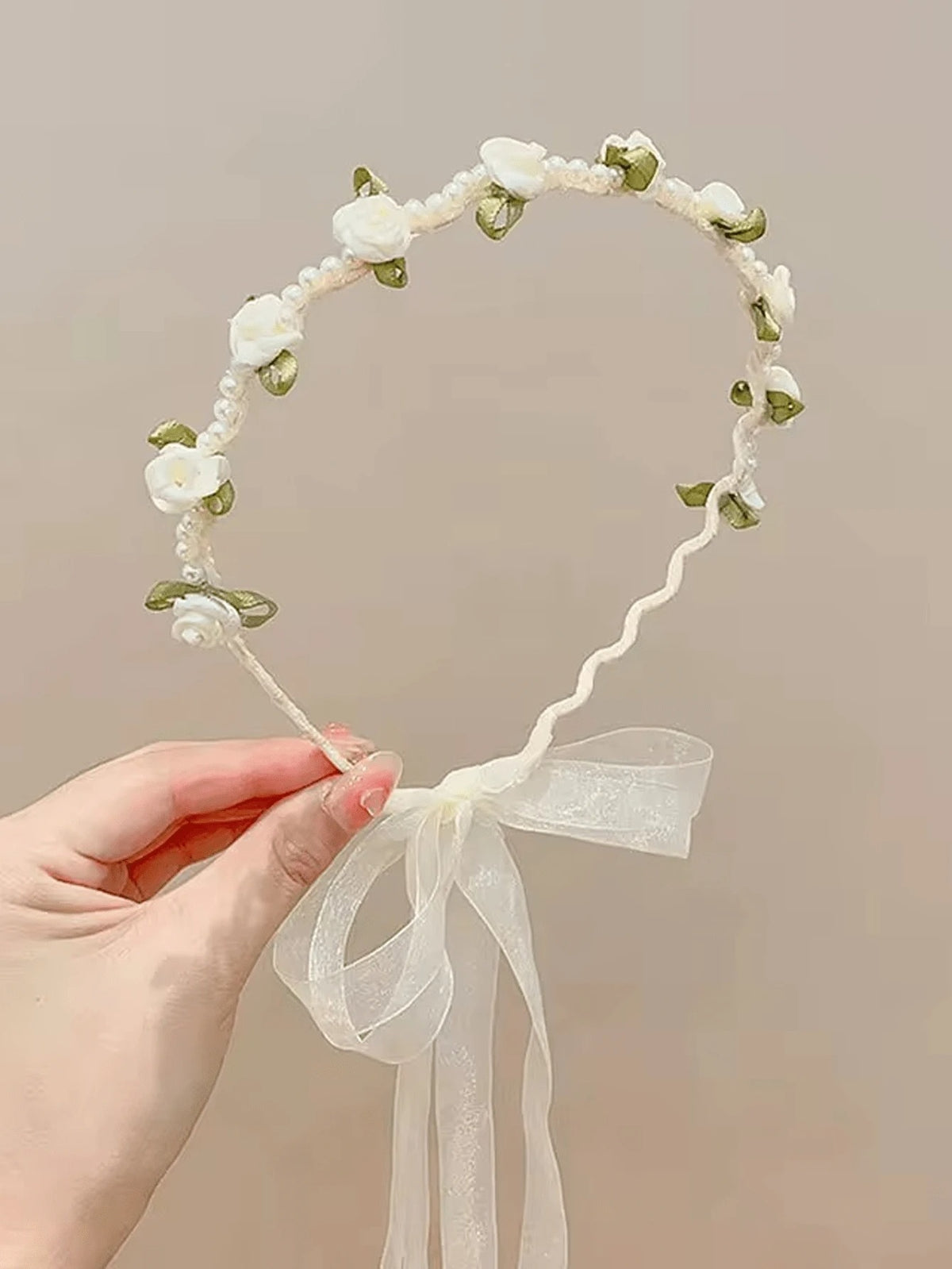 Floral headband with a bow held by a hand against a beige background