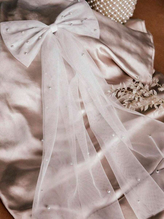 Light pink fabric with a large bow and pearl embellishments on a neutral background