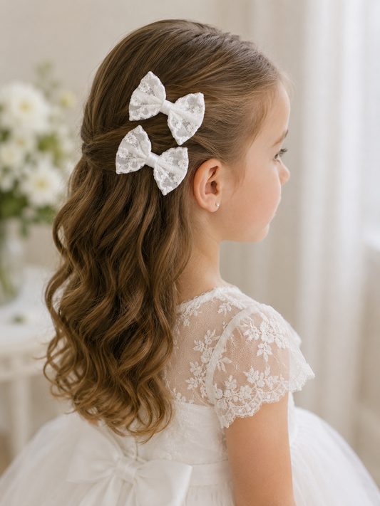 Young girl with styled hair featuring lace bow hair accessories, wearing a white dress.