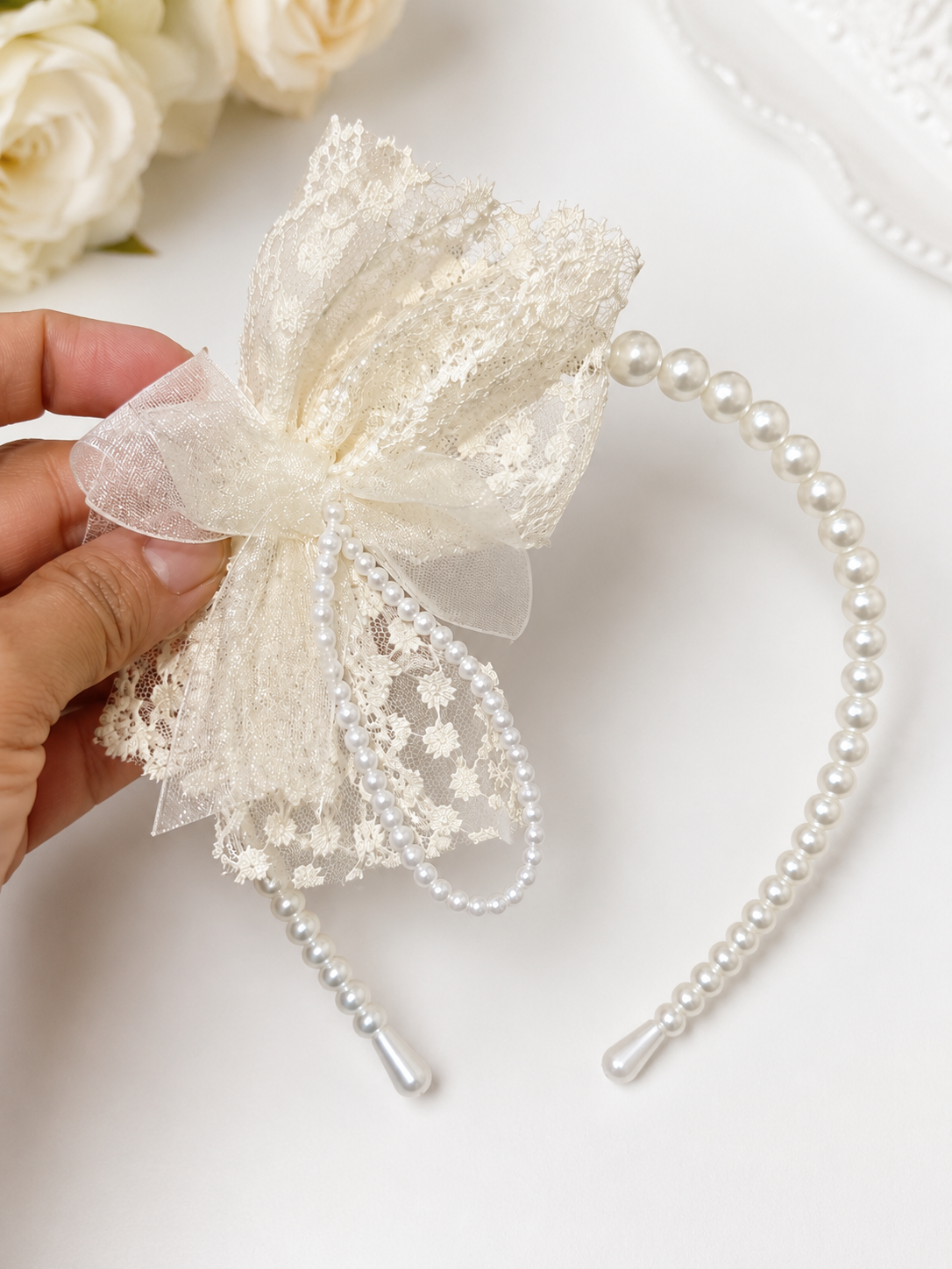 Pearl headband with decorative bow held by a hand on a white background
