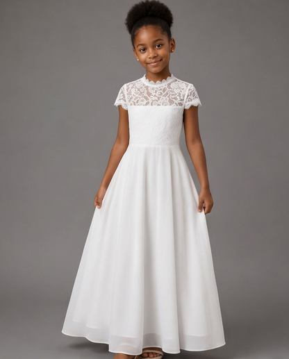 A young girl wearing a white formal dress with a lace high neck and cap sleeves, standing against a solid gray studio background.