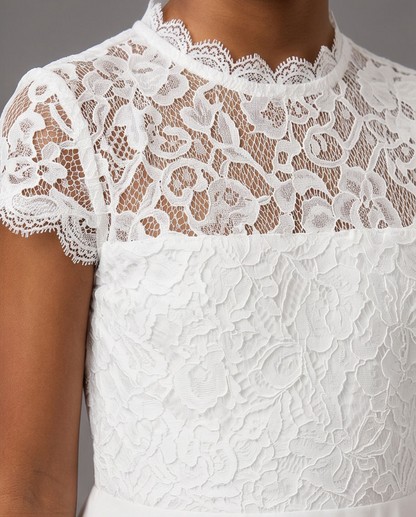 Close-up of a white lace dress with a floral lace bodice, short lace sleeves, and a sheer floral lace yoke over the skin, shown on a model.