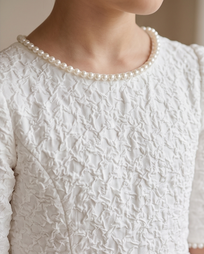 A close-up of a person wearing a white textured lace top with a pearl collar and a matching pearl necklace.