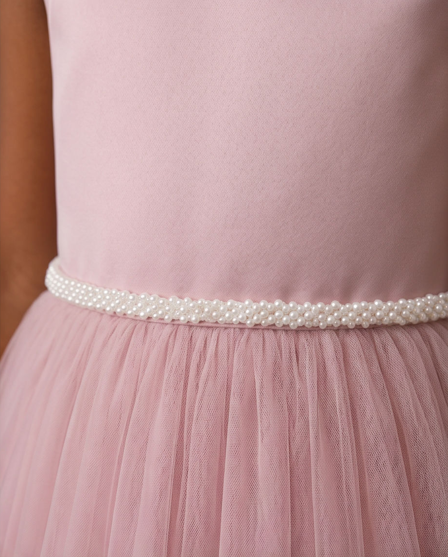 Close-up of a dusty pink dress with a smooth satin bodice and a pleated tulle skirt, featuring a decorative waistband of white faux pearls.