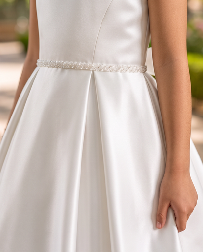 Close-up of a white satin wedding dress with a beaded waistband and a model's hand holding the skirt.