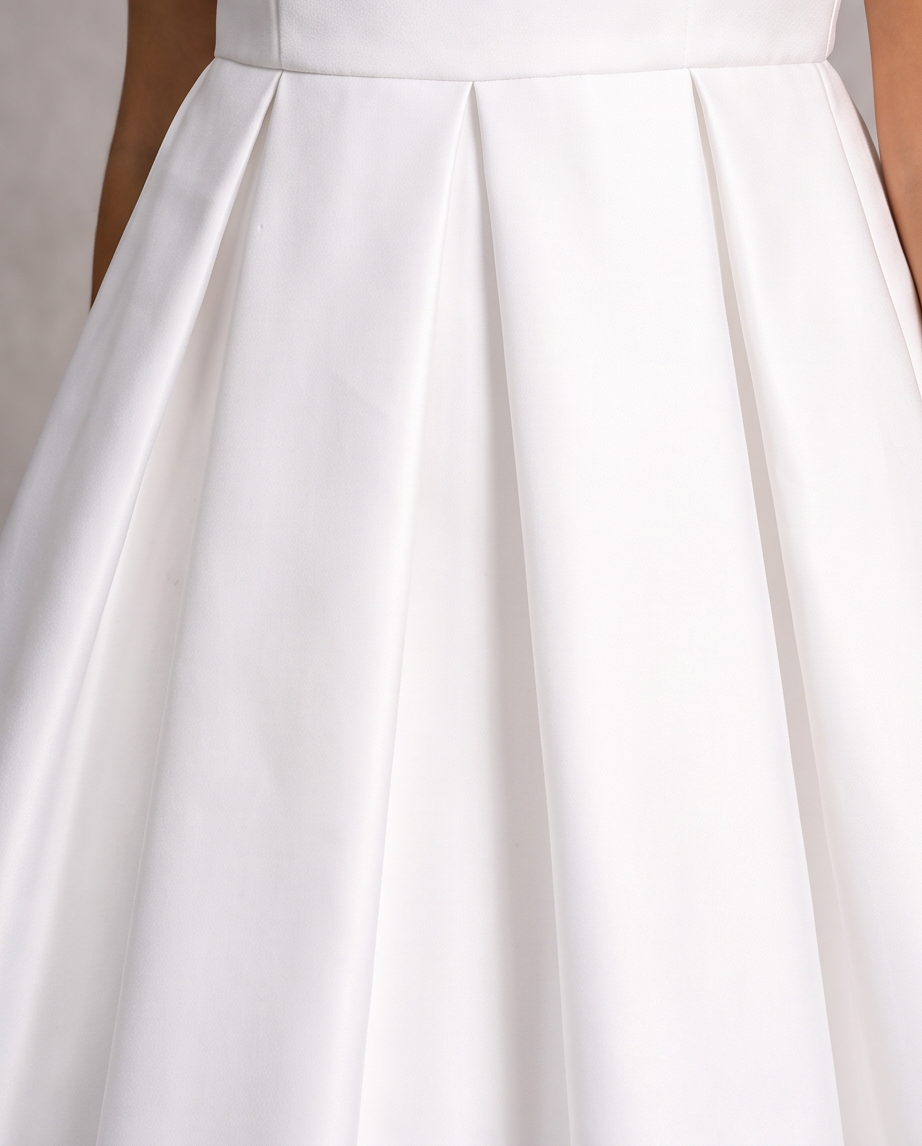 Close-up of a white satin or silk pleated skirt with a structured waistband, showing the fabric's soft sheen and elegant folds.