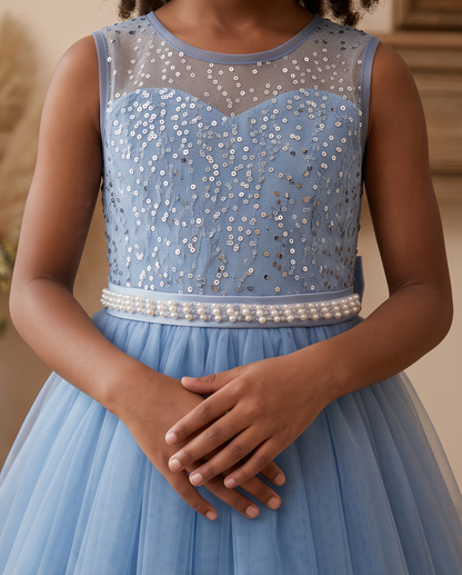 A sleeveless light blue formal dress with a sheer mesh bodice, silver sequin embellishments, a pearl-beaded waistband, and a flowing tulle skirt, shown on a child with hands clasped in front.