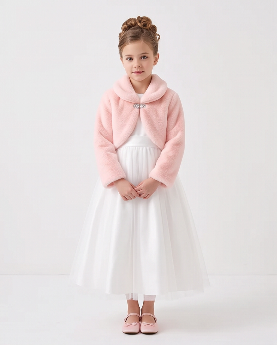 A young girl with her hair in two buns stands against a plain white studio background, wearing a light pink fuzzy cropped jacket with a silver button over a white tulle dress and pink shoes.