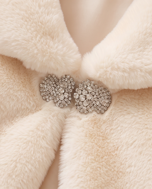 Close-up of a cream faux fur coat with two heart-shaped crystal brooch closures at the center front.