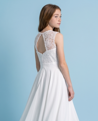 A young woman wearing a white sleeveless dress with a lace open-back bodice and a flowing skirt, photographed against a light blue studio background.