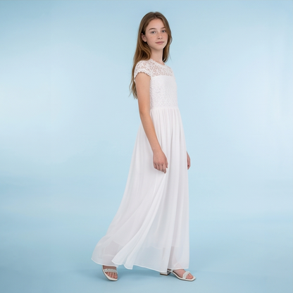 A young girl modeling a long white maxi dress with a lace bodice and cap sleeves, standing against a light blue studio background.