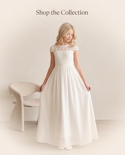 A young blonde girl wearing a long white A-line dress with a lace bodice and cap sleeves, standing in a studio setting next to a modern curved chair. The text 'Shop the Collection' is printed at the top of the image.