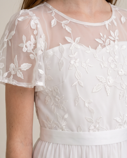 Close-up of a white dress with floral lace applique and sheer flutter sleeves, worn by a model.
