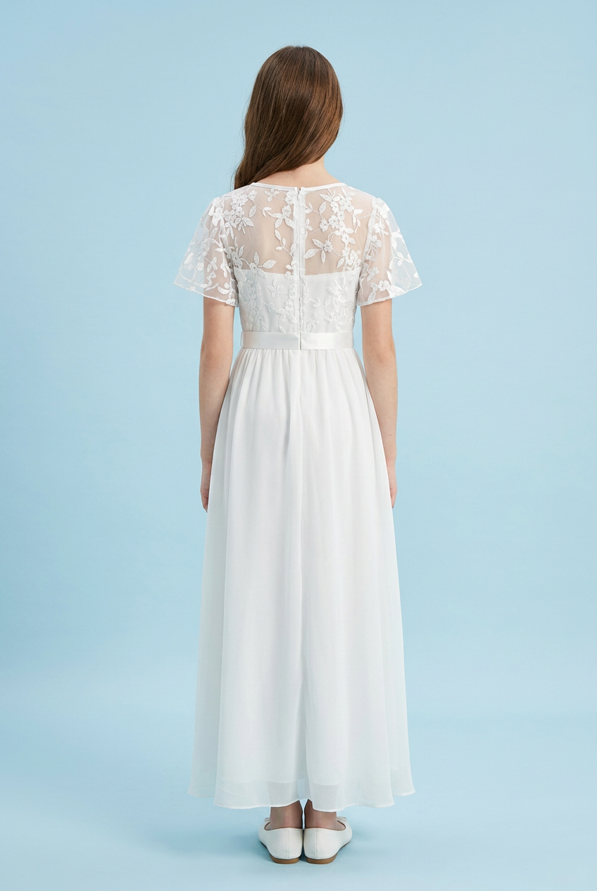 A woman viewed from the back wearing a white maxi dress with sheer floral lace short sleeves, a lace back panel, a defined waist, and a flowing chiffon skirt, against a light blue studio background.