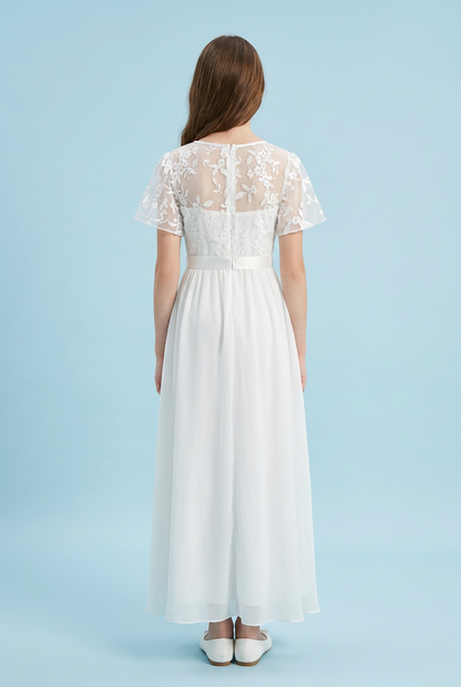 A woman viewed from the back wearing a white maxi dress with sheer floral lace short sleeves, a lace back panel, a defined waist, and a flowing chiffon skirt, against a light blue studio background.