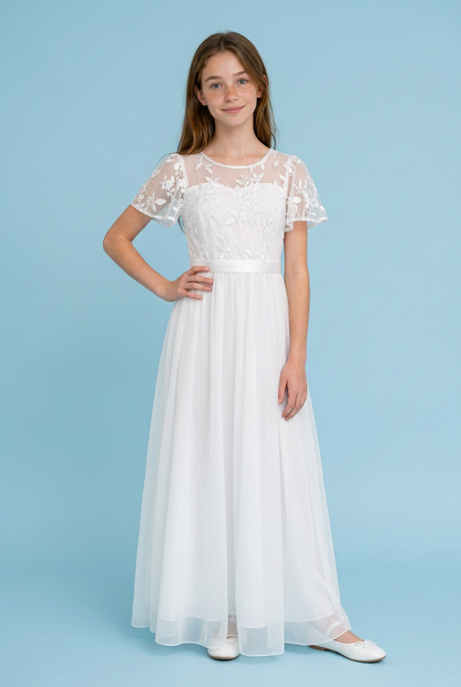 A young girl modeling a long white lace and tulle formal dress with short flutter sleeves, standing against a solid light blue studio background.