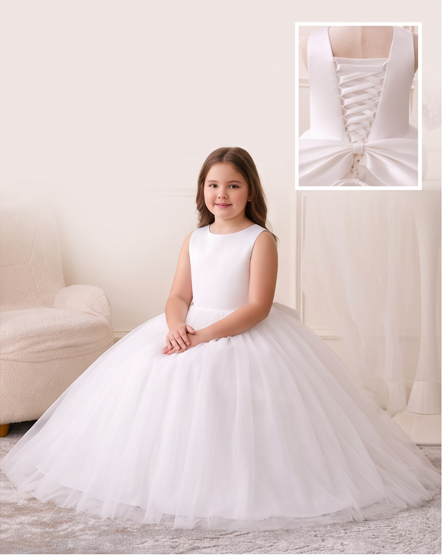 A young girl wearing a sleeveless white ball gown with a full tulle skirt, seated indoors. The image includes an inset close-up of the back of the dress showing lace-up detailing and a bow.