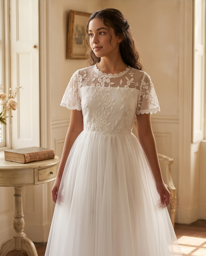 A girl stands on a sunlit garden path wearing a white lace midi dress with ruffled cap sleeves, a high neckline, and a full skirt. 