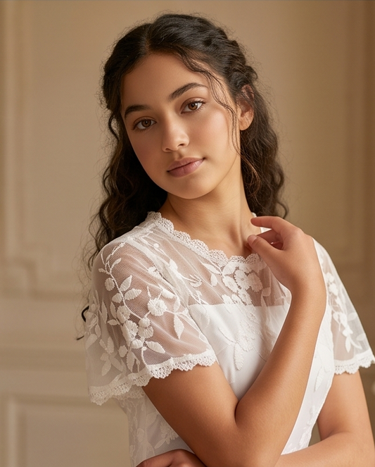 A girl stands on a sunlit garden path wearing a white lace midi dress with ruffled cap sleeves, a high neckline, and a full skirt. 