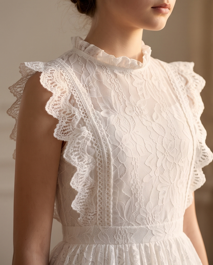 Close-up of a woman wearing a white lace dress with ruffled trim and a high ruffled neckline, photographed against a soft beige background.
