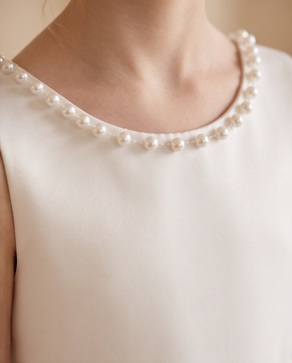 A close-up of a model wearing a white sleeveless top with a delicate collar of white faux pearls.