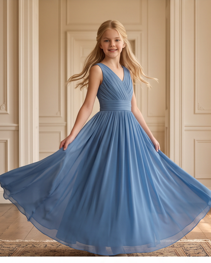 A young girl with blonde hair wearing a sleeveless, V-neck blue dress with a pleated skirt, posing in a grand room with beige walls and wooden floors. The bottom of the image features a white banner with the text 'BOOK YOUR A.
