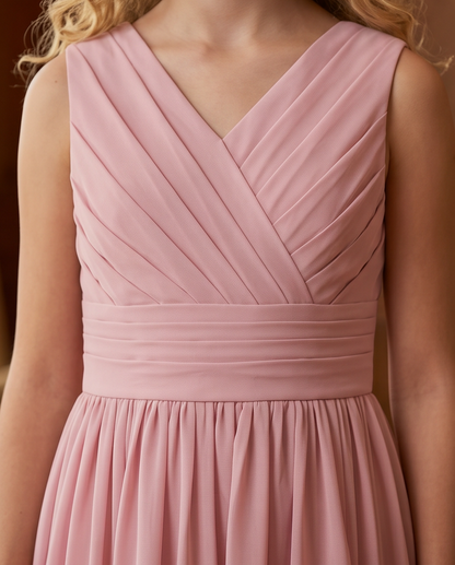 A close-up of a sleeveless dusty pink dress with a V-neckline, pleated bodice, and gathered waistband, shown on a model.