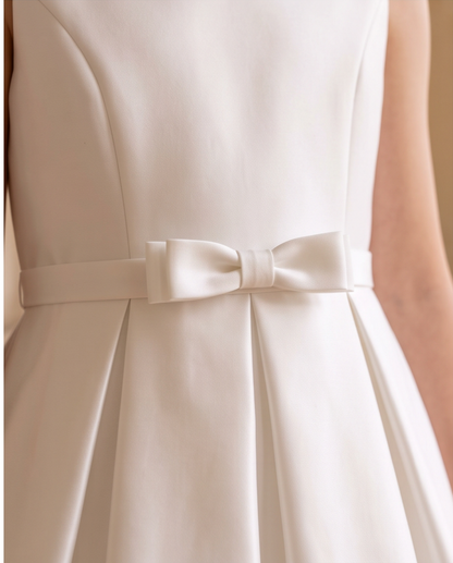 Close-up of a sleeveless ivory dress with a satin waist belt and bow detail, shown on a model.
