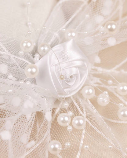 Close-up of white satin rose centre with scattered pearl sprays and tulle netting on fascinator