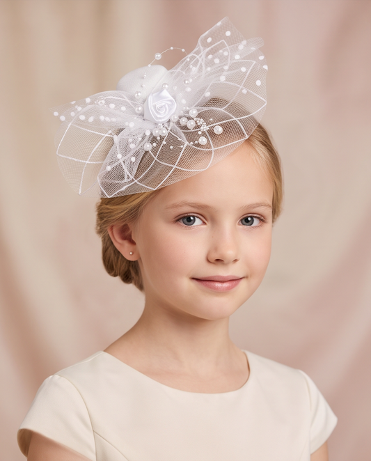 Girl wearing white pearl and rose fascinator with layered tulle netting, front face view in ivory dress