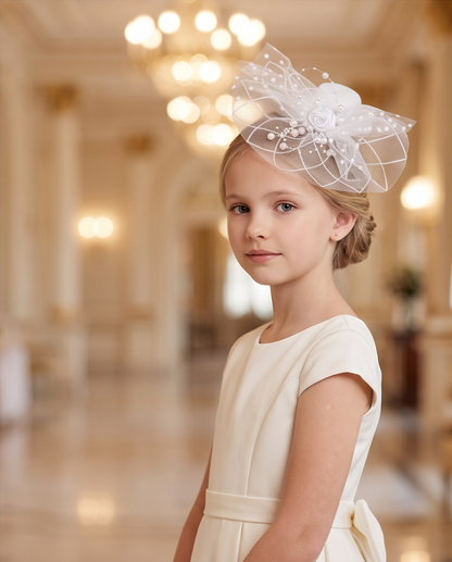 Girl wearing white pearl and rose fascinator with tulle netting in grand ballroom, three-quarter view in ivory dress