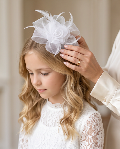 Adult placing white rose tulle fascinator with feathers on girl's head, close-up styling view