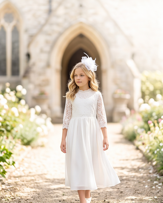 Girl wearing white rose tulle fascinator with feathers outdoors in front of church, full length view in white lace communion dress