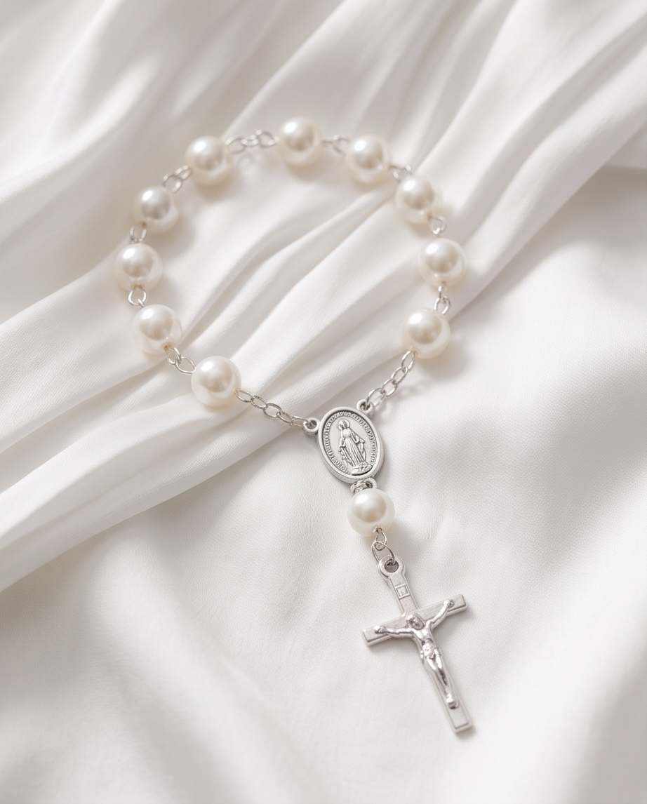 White pearl rosary bracelets with silver crucifixes on white satin with gift boxes and organza bags, top-down view
