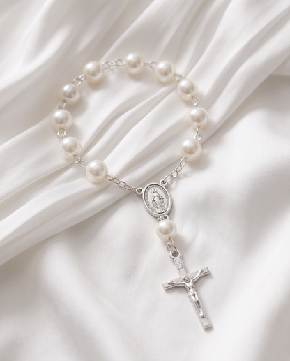 White pearl rosary bracelets with silver crucifixes on white satin with gift boxes and organza bags, top-down view
