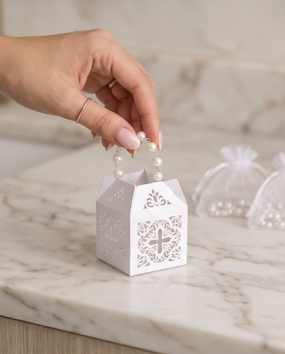 Multiple white pearl rosary bracelets with silver crucifixes laid on white satin with laser-cut gift boxes and organza bags