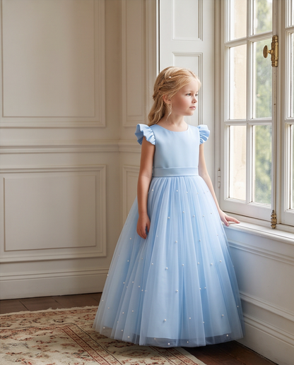 Girl in blue pearl tulle floor-length communion dress standing by window