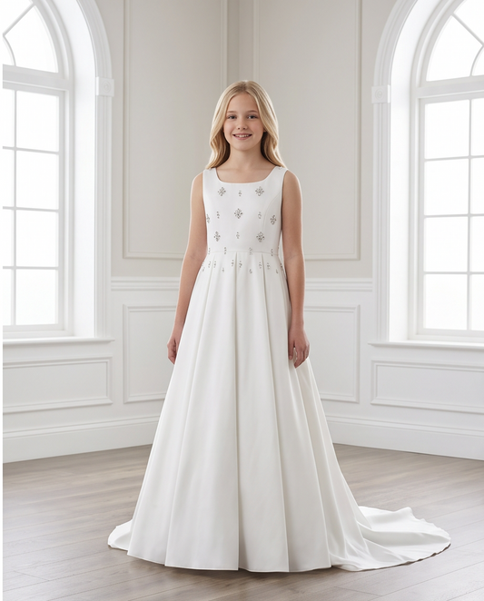 A young girl stands in a bright, elegant room wearing a sleeveless white A-line dress with delicate silver floral embroidery on the bodice and a slight train.