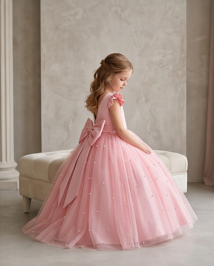 Girl wearing pink pearl tulle flower girl dress with V-back satin bow front view indoors