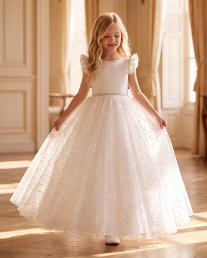Girl wearing white glitter tulle ball gown back view showing V-back and satin bow with floral arch