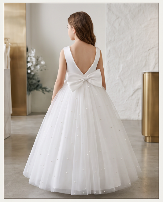 Young girl sitting wearing white pearl neckline tulle dress holding flowers side view