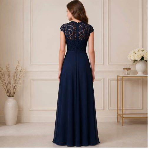 A woman stands with her back to the camera wearing a floor-length navy evening gown with a lace lace bodice and cap sleeves, set against a classic cream paneled wall with decorative vases and a side table.
