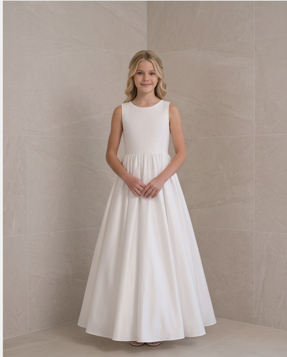 A young girl stands in a sleeveless white A-line dress with a fitted bodice and full skirt, posing in front of a beige tiled wall.