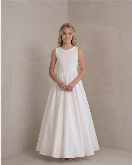 A young girl stands in a sleeveless white A-line dress with a fitted bodice and full skirt, posing in front of a beige tiled wall.