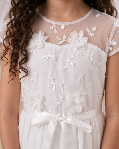 White floral embroidered dress with a sheer mesh neckline, short sleeves, and a satin ribbon bow at the waist, shown on a model.