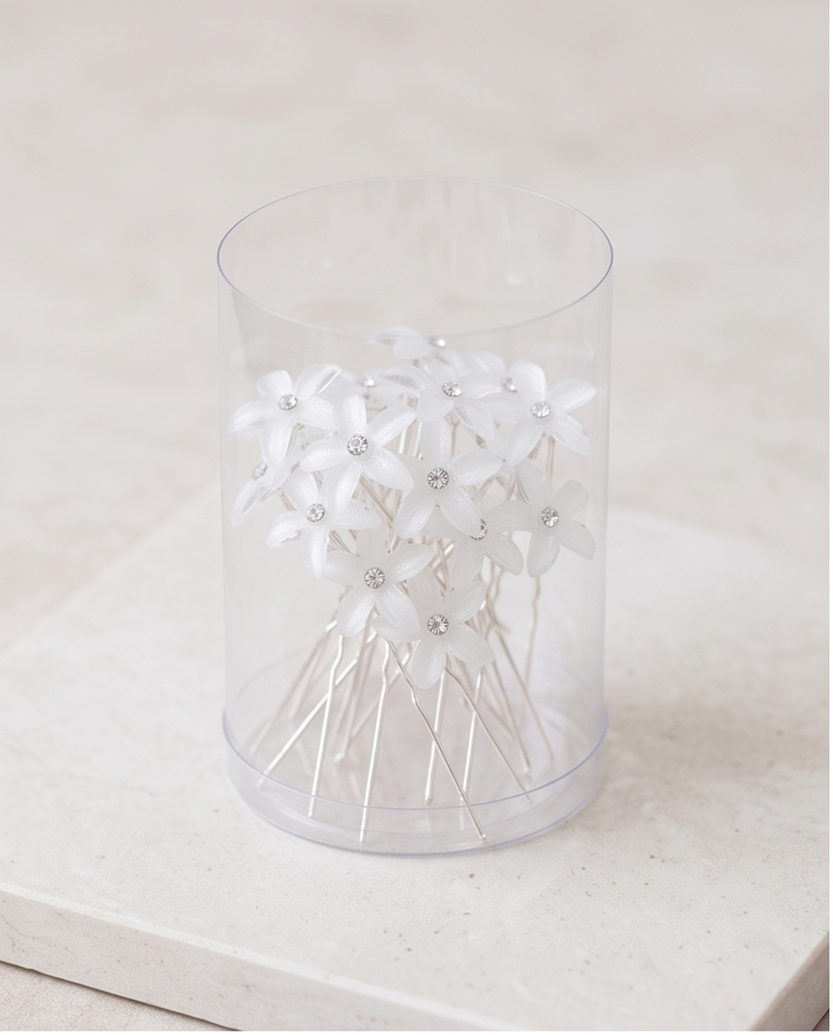 Five white flower hair pins arranged on fabric