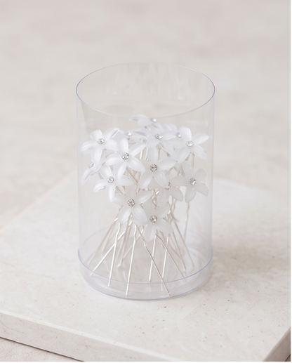 Five white flower hair pins arranged on fabric